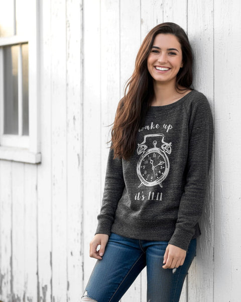 Woman wearing a heather charcoal wide‑neck sweatshirt with a vintage 11:11 angel number clock design.